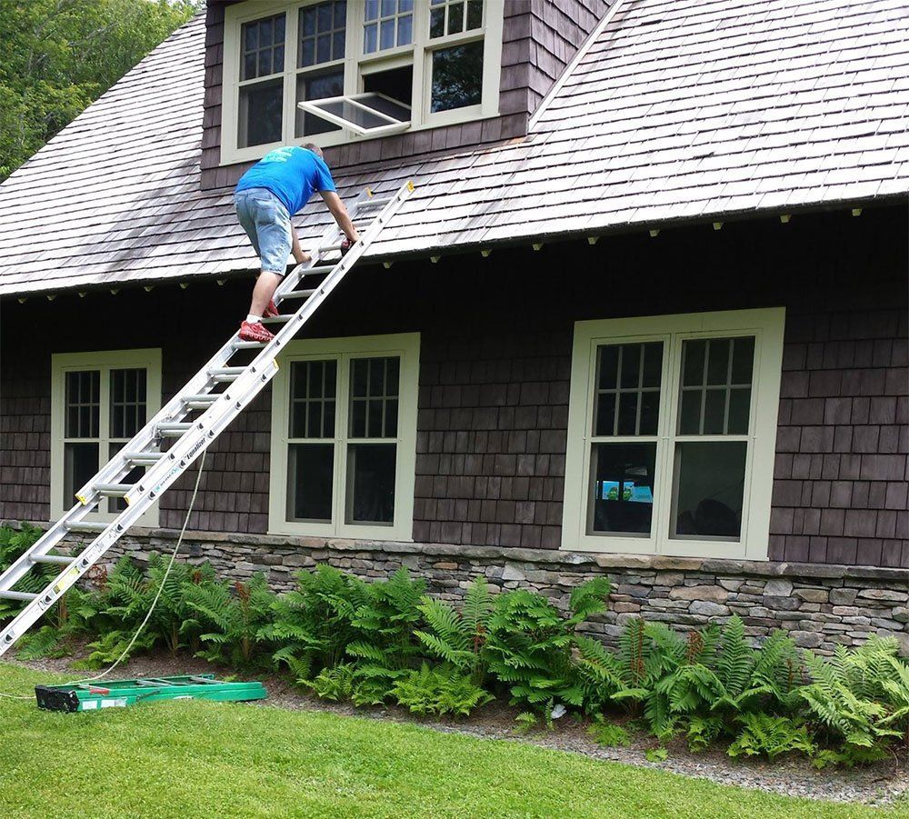 A man on a ladder is working on the roof of a house