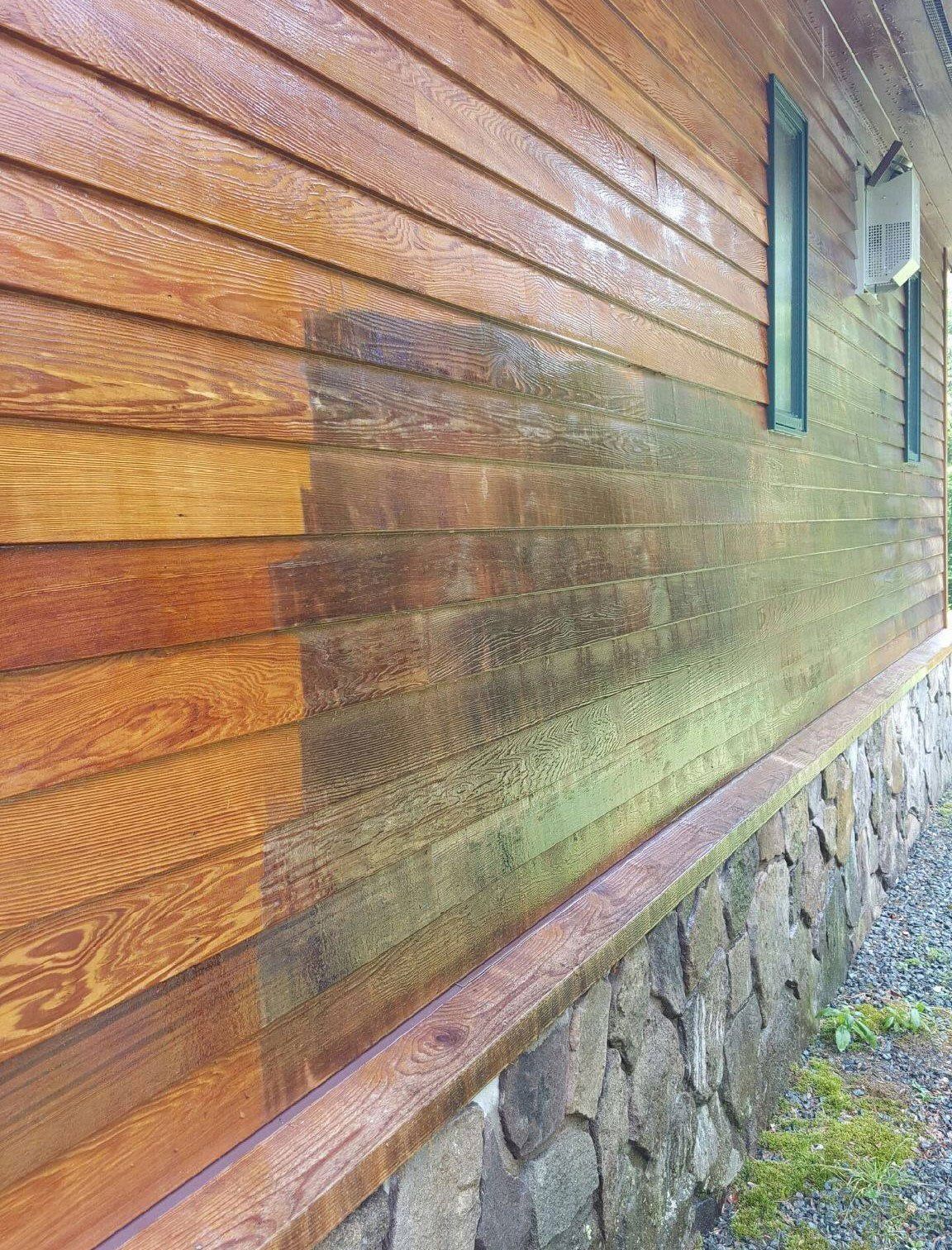 The side of a wooden house is being cleaned and painted.