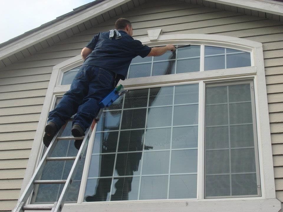 A man on a ladder is cleaning a window