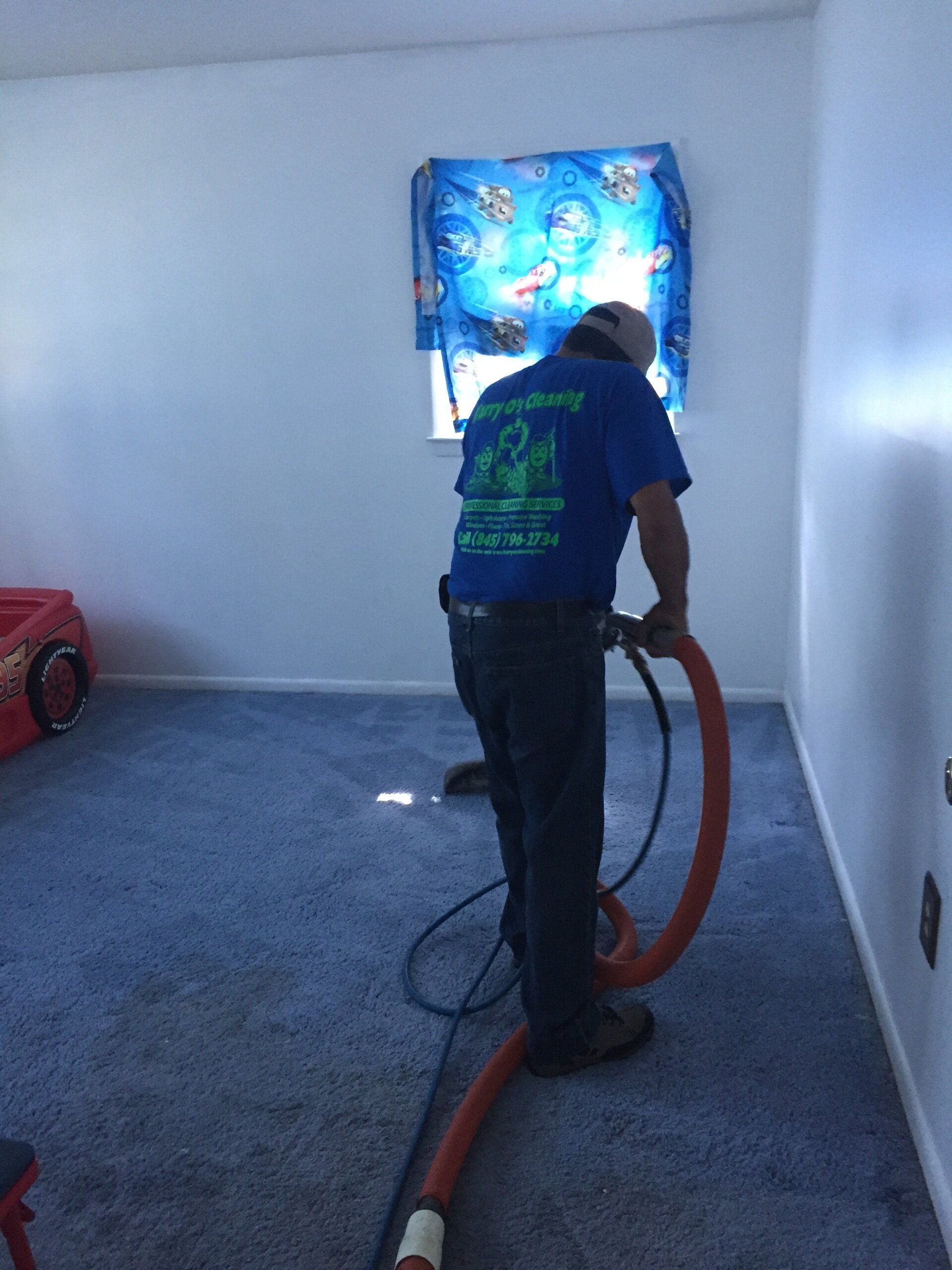 A man in a blue shirt is vacuuming a carpet in a room.