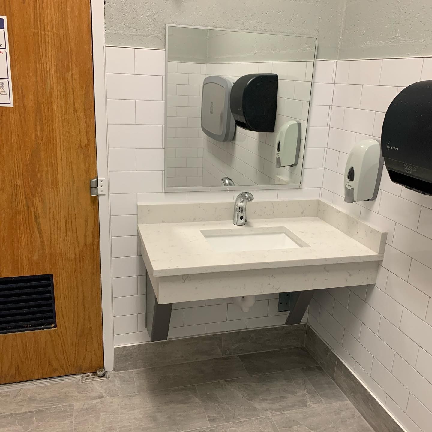 A bathroom with a sink , mirror and paper towels.