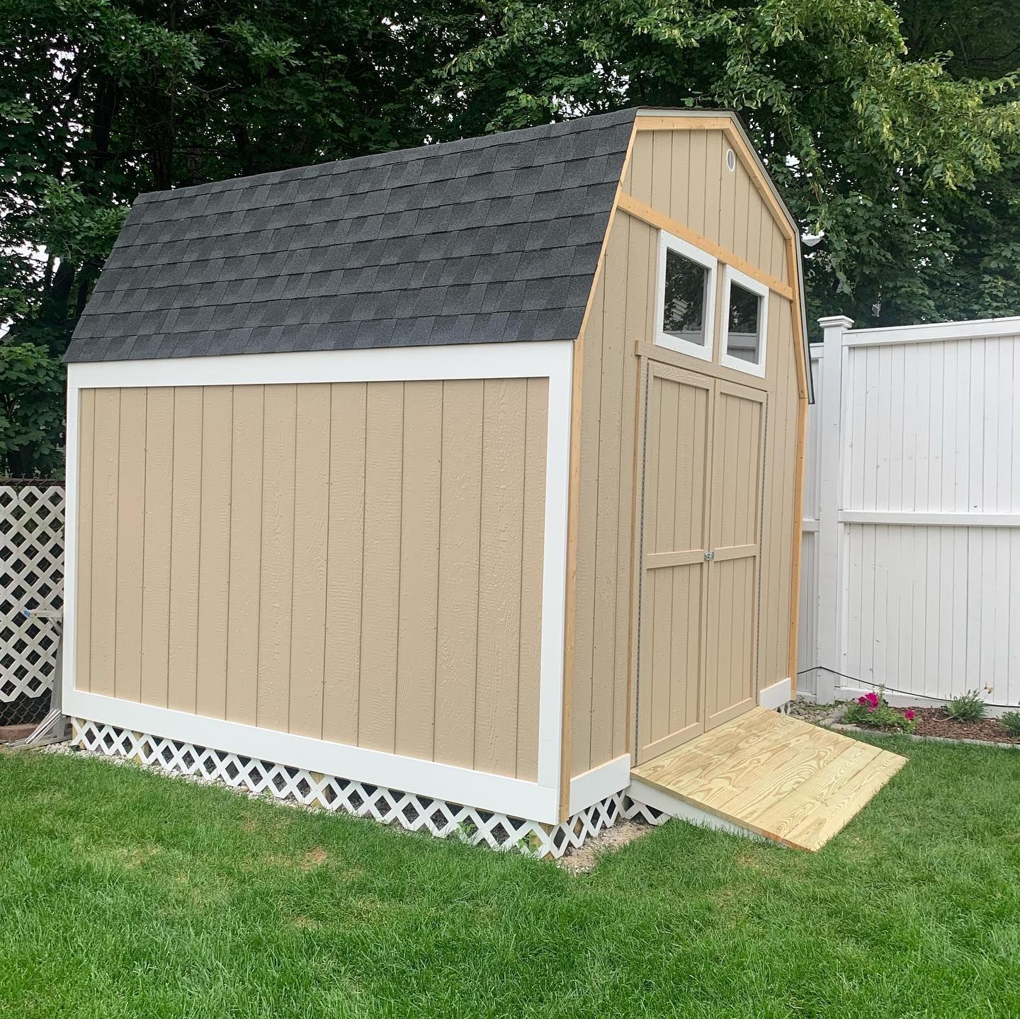 A brown shed with a black roof is sitting in the grass next to a white fence.