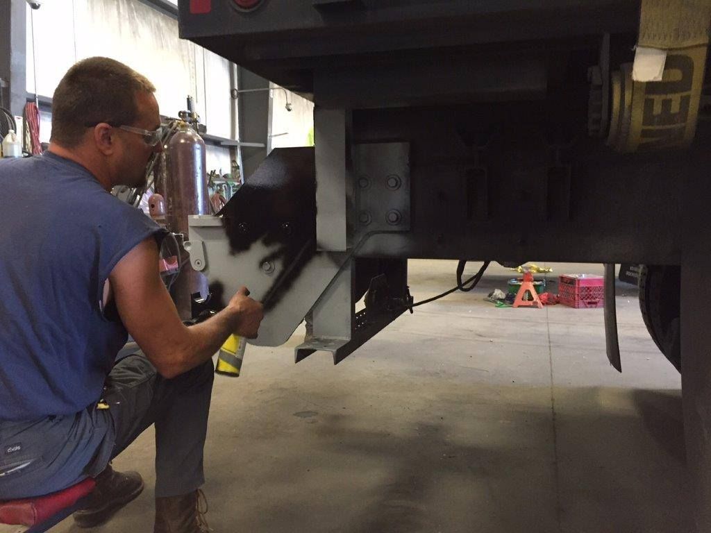 Mechanic working under a truck in a garage, inspecting the undercarriage with tools.