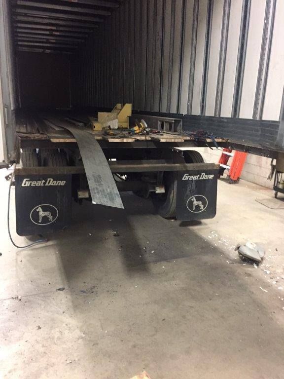 Flatbed trailer inside a truck trailer, with a gray ramp or metal sheet hanging off the back.