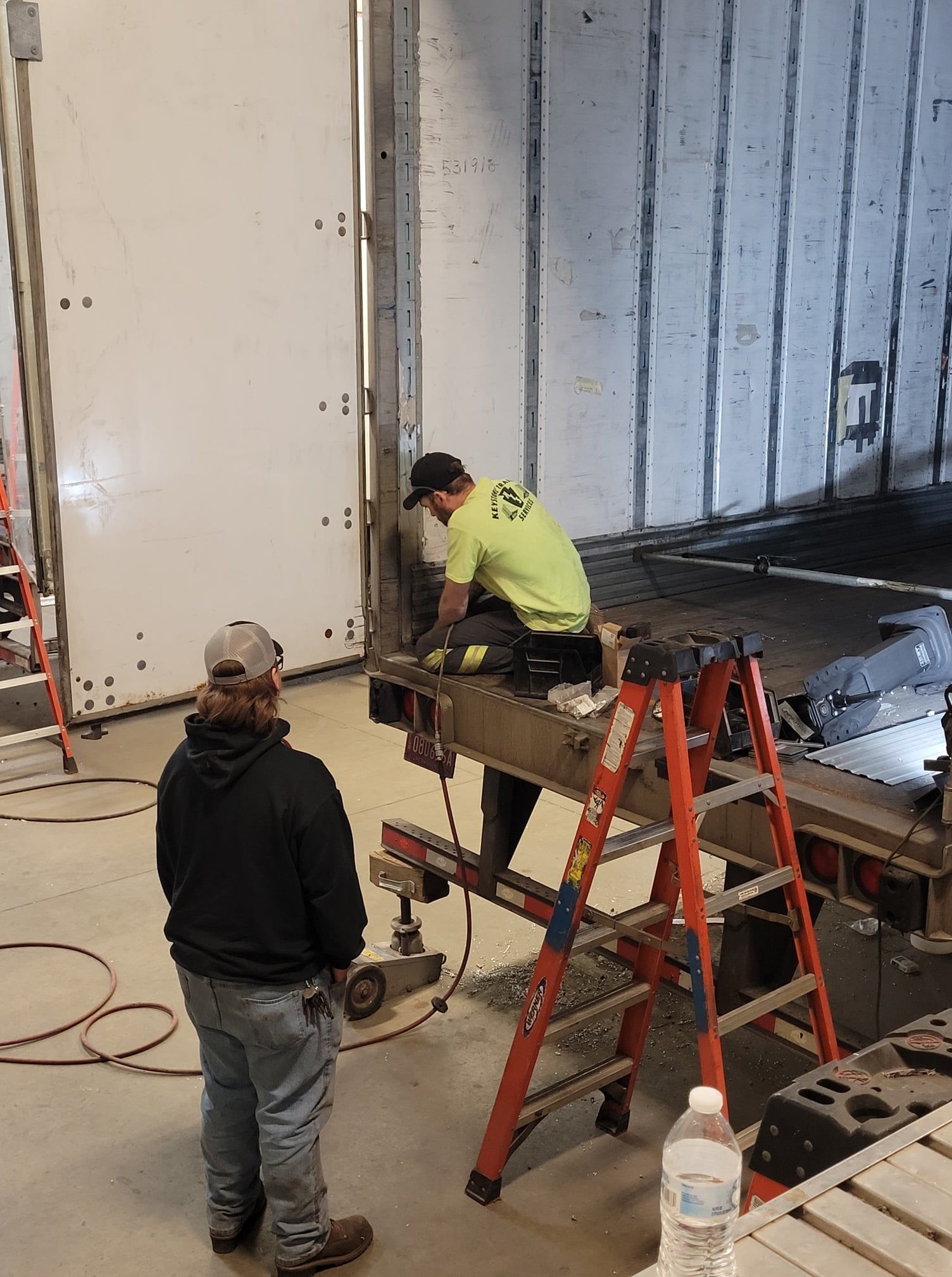 Workers on a ladder and scaffold installing a large wall panel inside a construction site.