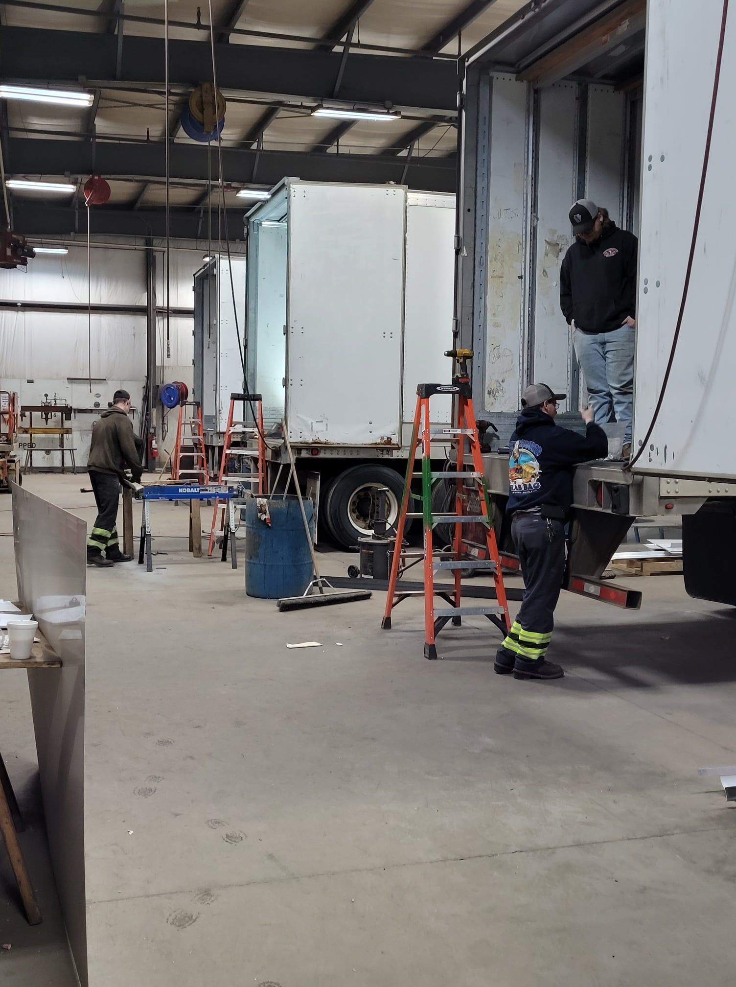 Workers loading a white truck inside a warehouse, with ladders and equipment nearby.