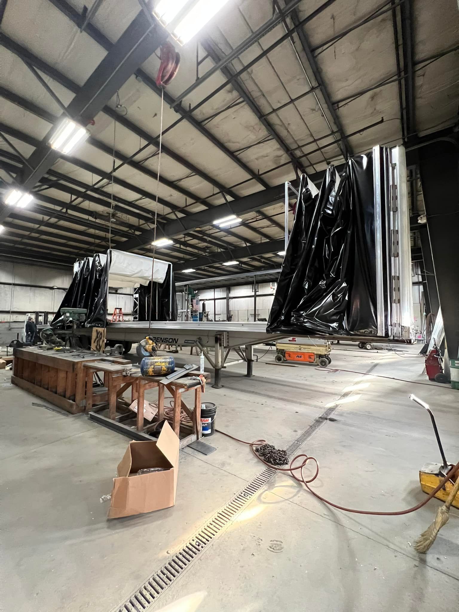 Large industrial warehouse with tall black hanging curtains, scaffolding, and tools on a concrete floor.