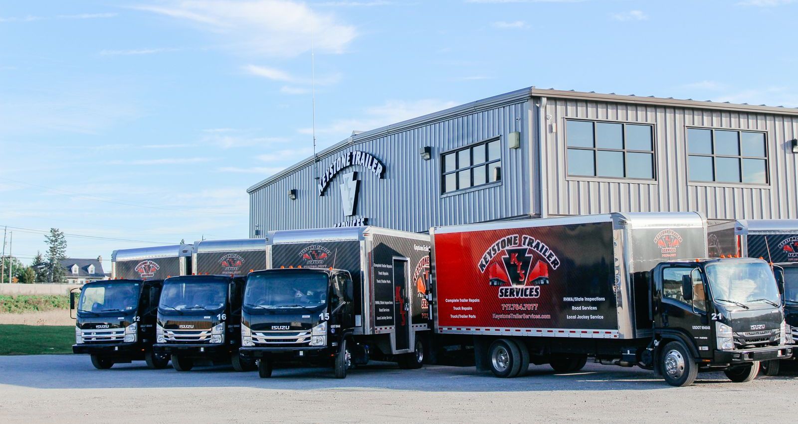 Four delivery trucks were parked in front of a large metal warehouse on a sunny day.