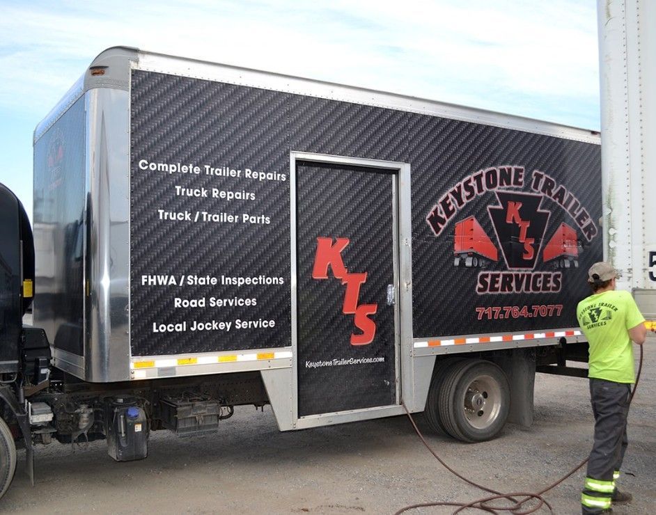 Keystone Trailer Service truck with red logo; worker in neon shirt nearby.