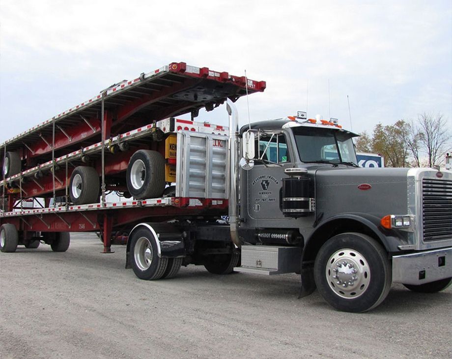 Silver semi truck hauling a red car carrier trailer loaded with vehicles on a road