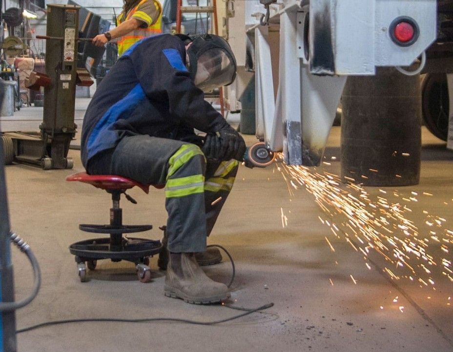 A worker in safety gear is grinding metal near a vehicle
