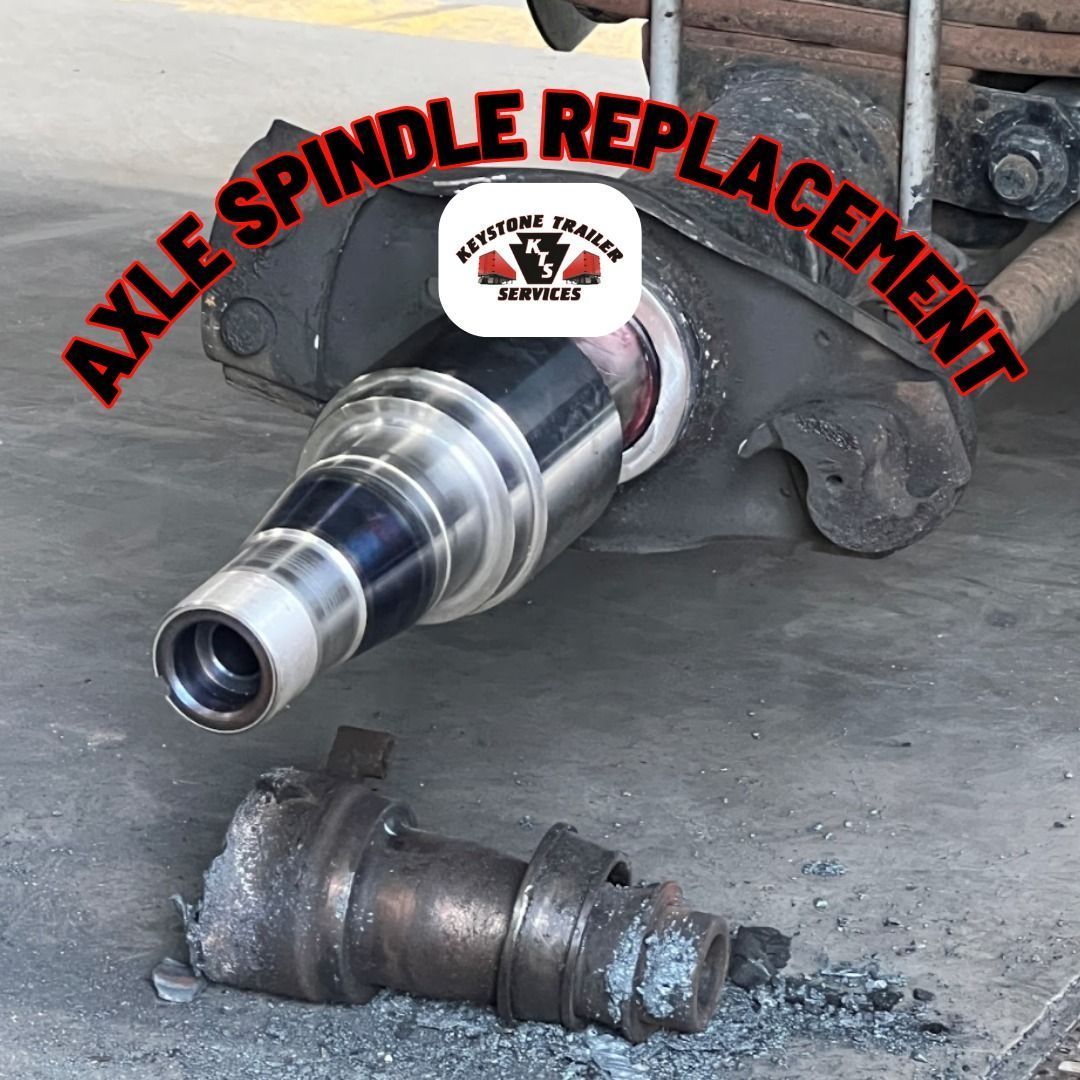 Damaged axle spindle beside a replacement spindle under a lifted vehicle