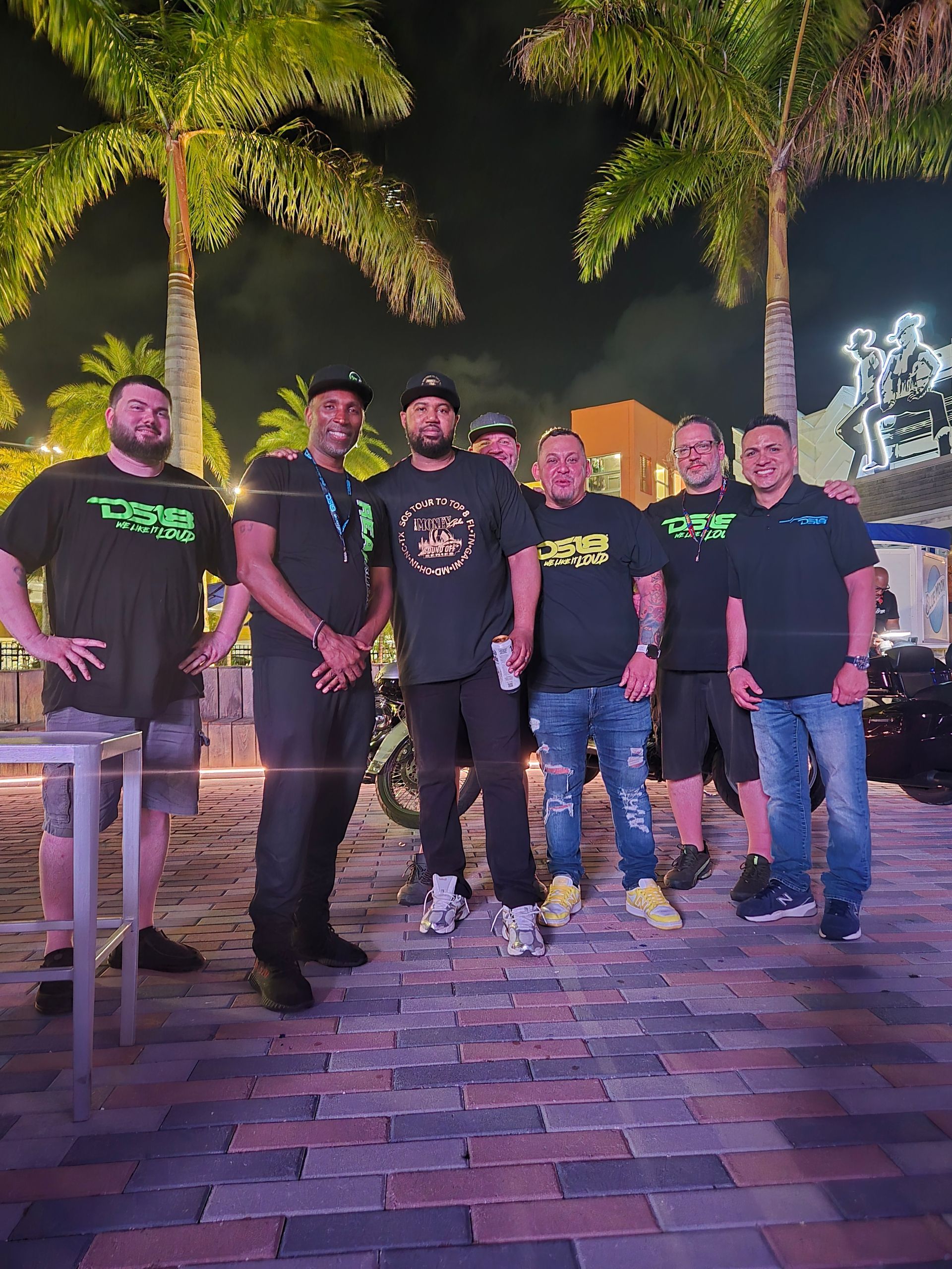 A group of men are posing for a picture in front of palm trees at night.