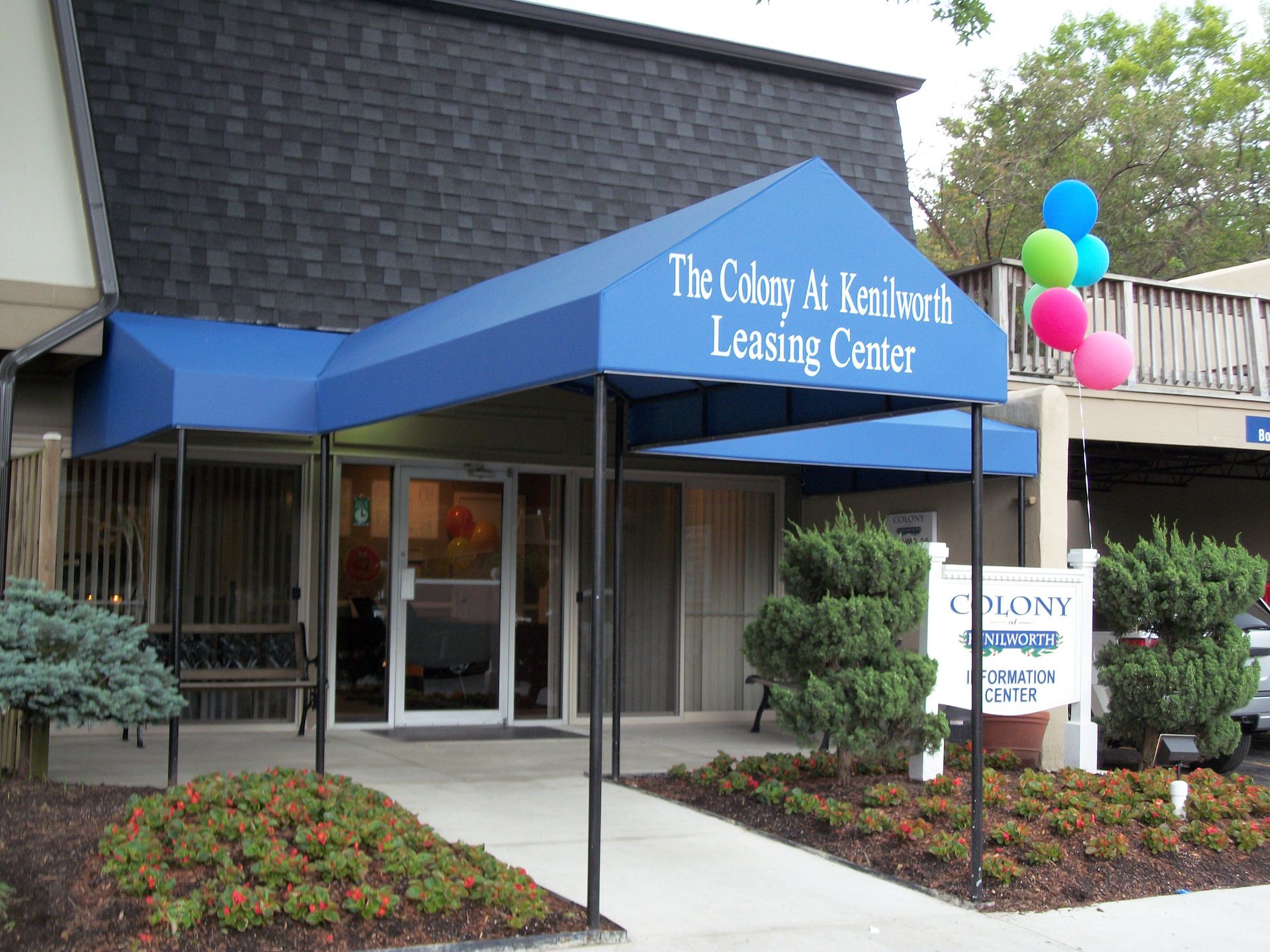 A building with a blue awning that says the colony apartment leasing center