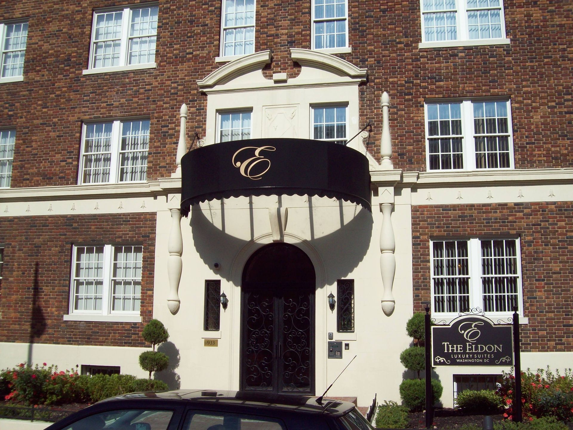 A car is parked in front of a brick building with a black awning over the entrance