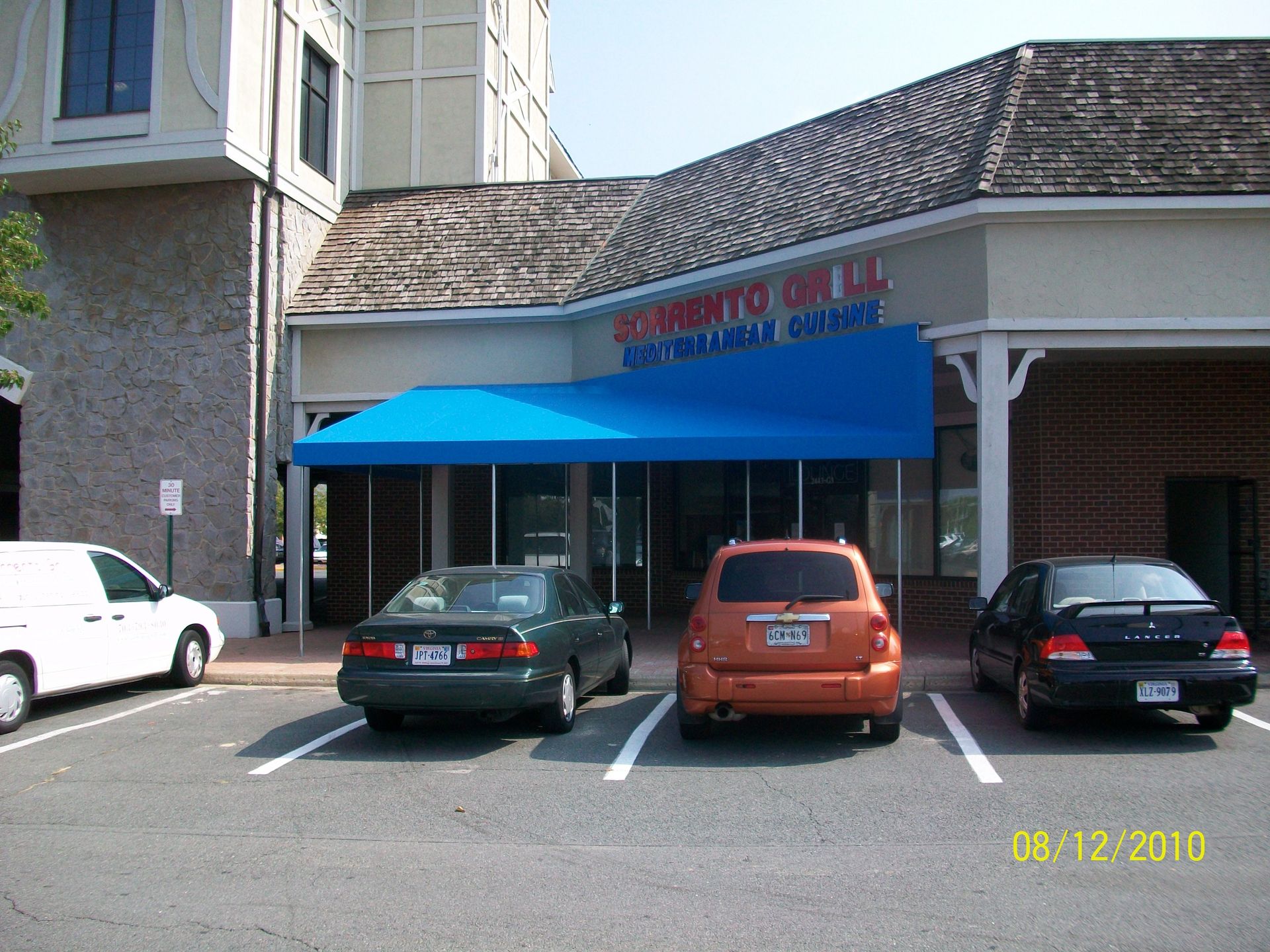 Cars are parked in front of a building with a blue awning