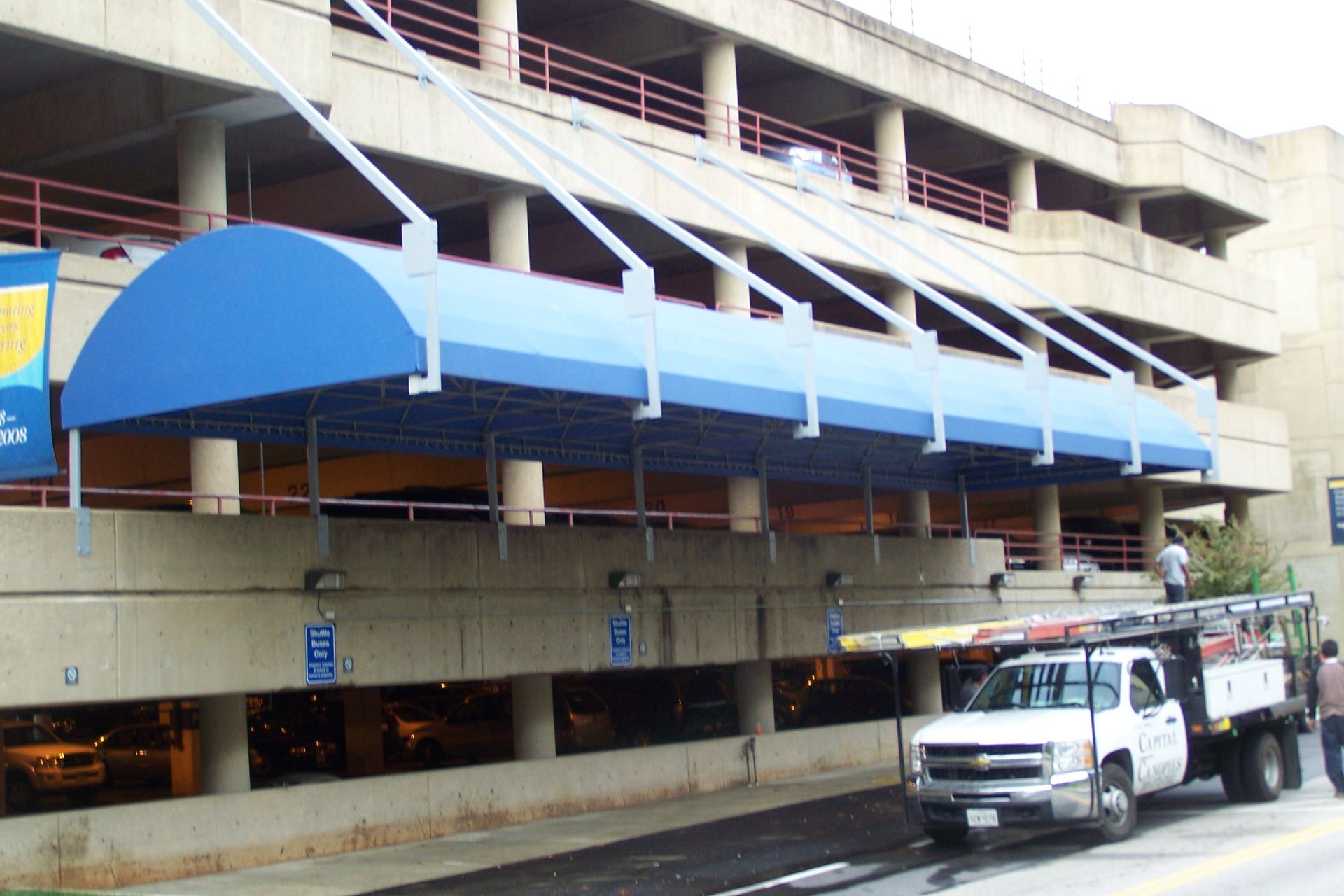 A white truck is parked under a blue awning in front of a parking garage