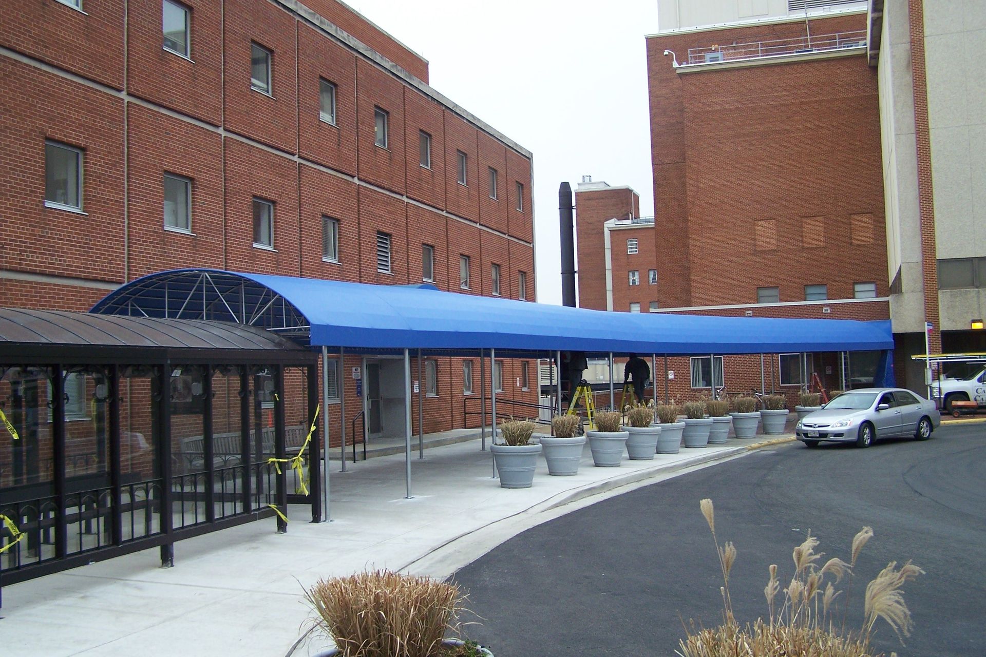 A car is parked under a blue awning in front of a brick building