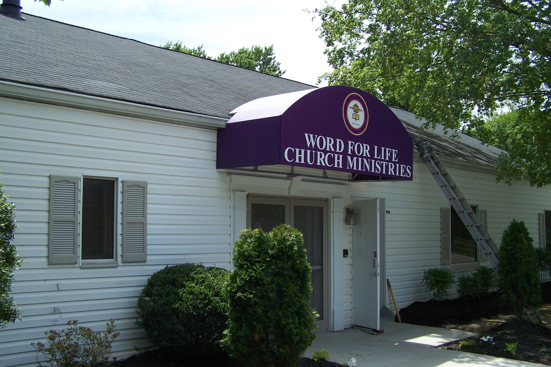 A white building with a purple awning that says word for life church ministries