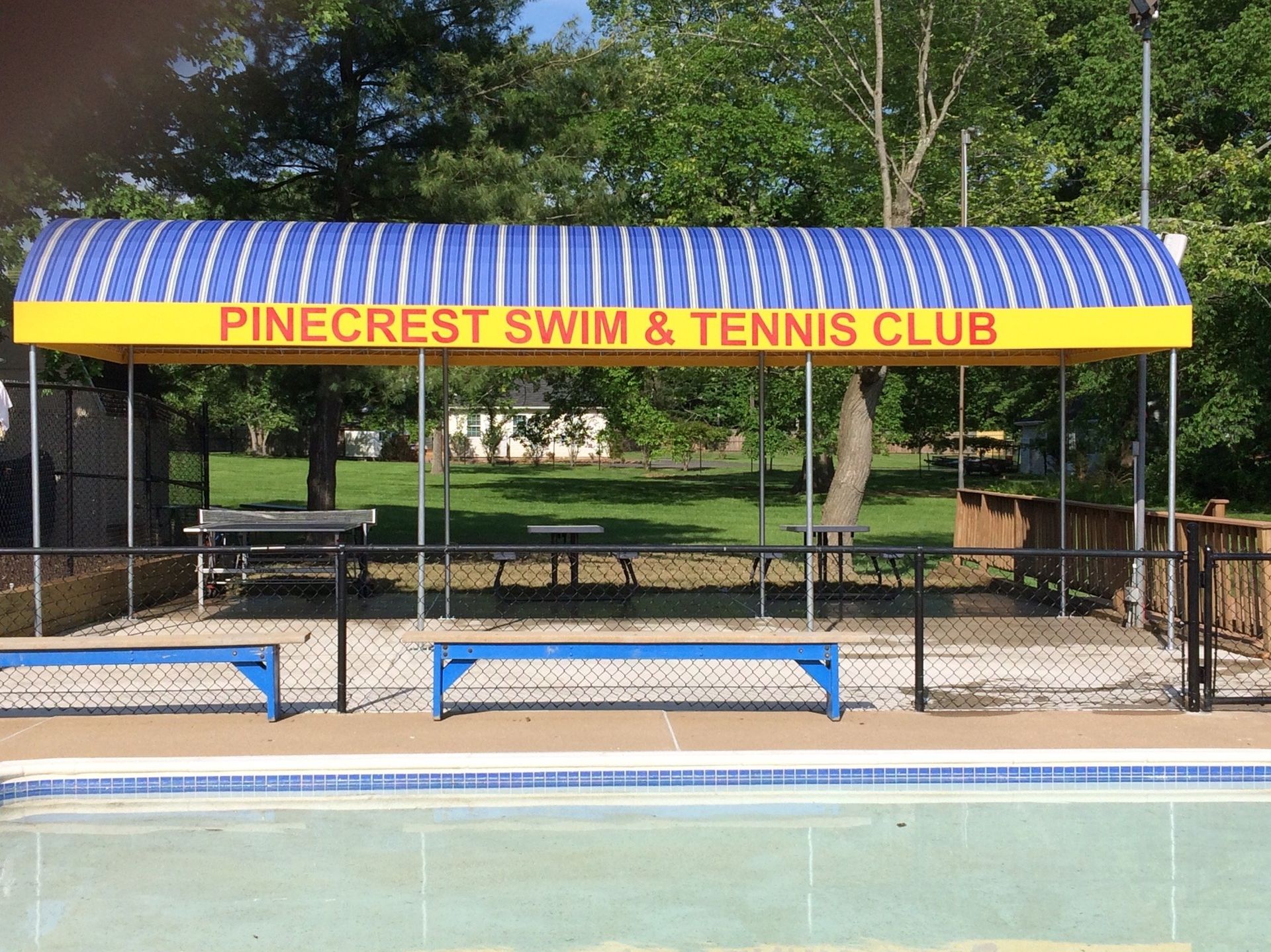 A blue and yellow awning over a swimming pool says Pinecrest Swim and Tennis Club