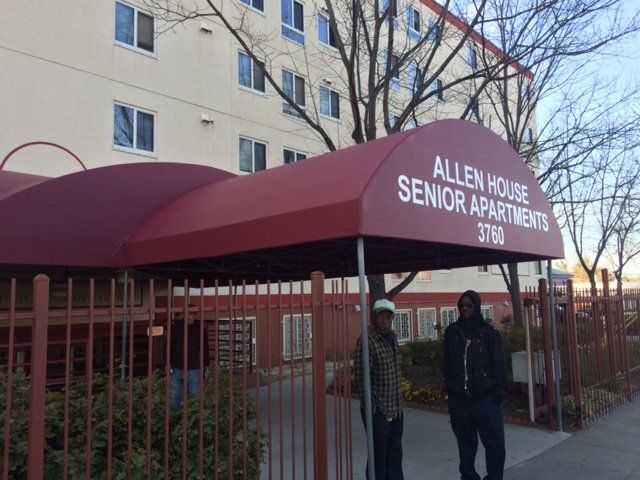 Two men standing under a canopy that says allen house senior apartments