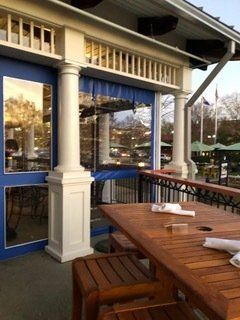 A wooden table with a napkin on it is on a porch in front of a building