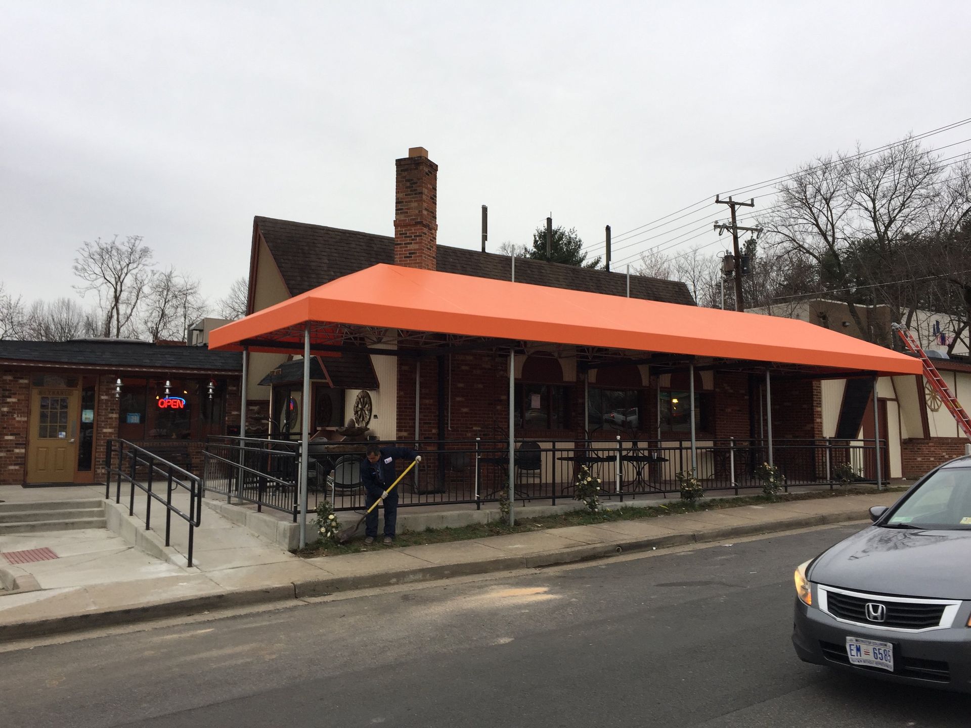 A car is driving past a restaurant with an orange awning.