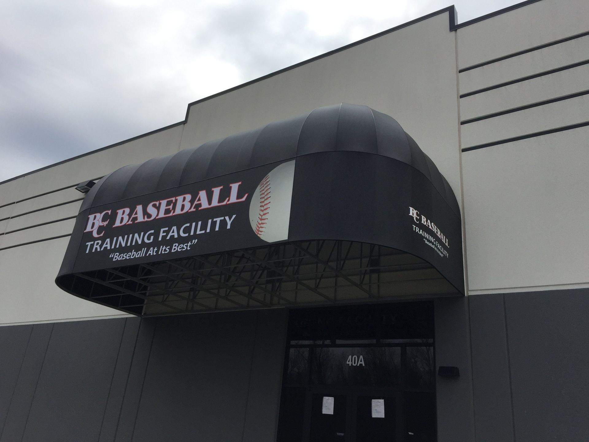 A black awning over the entrance to a baseball training facility.