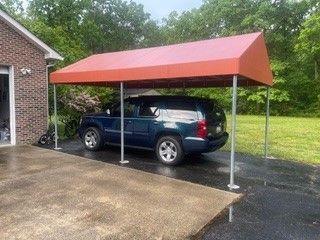 A blue suv is parked under a red canopy in a driveway
