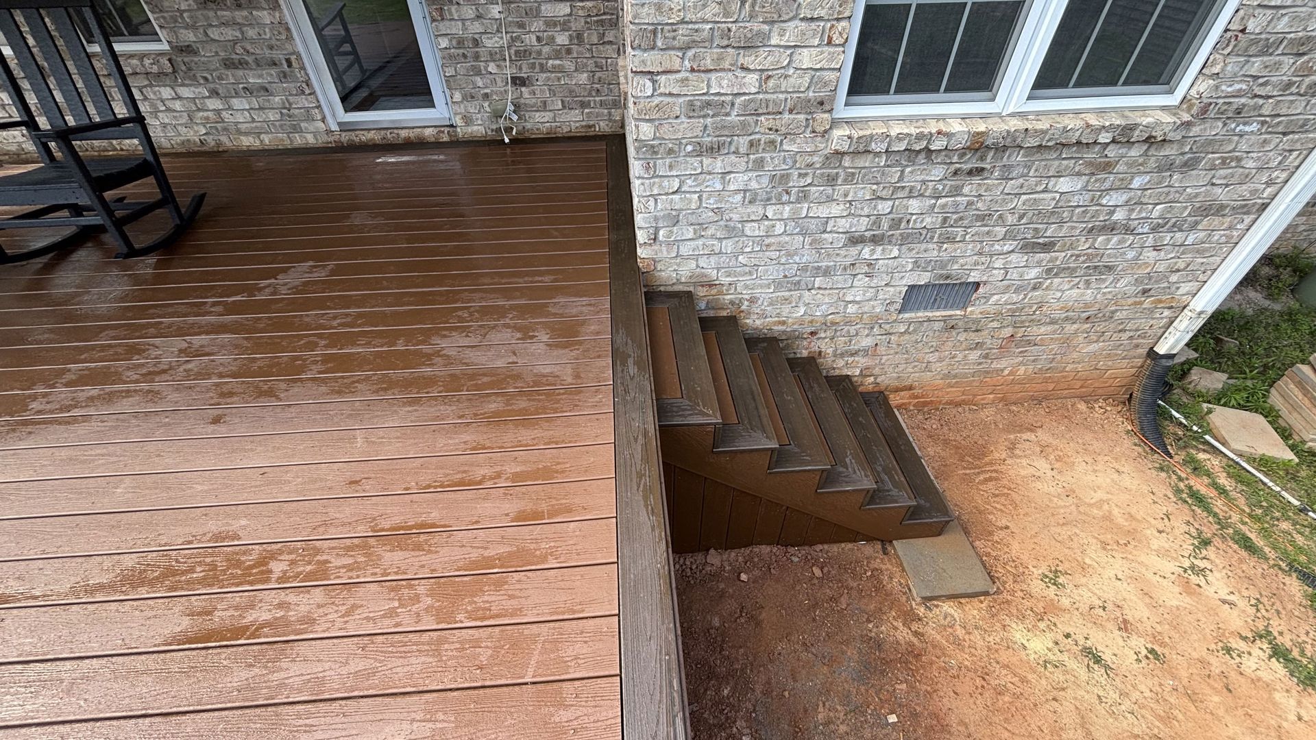A wooden deck with stairs leading up to a brick house.