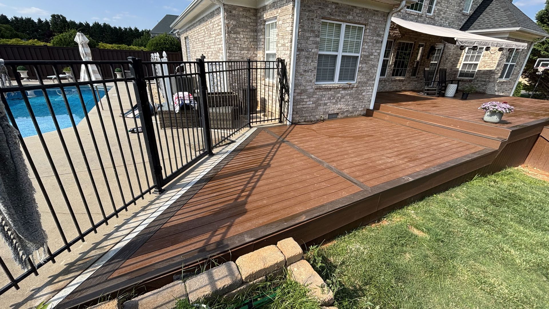 There is a fence around the deck and a swimming pool in the background.
