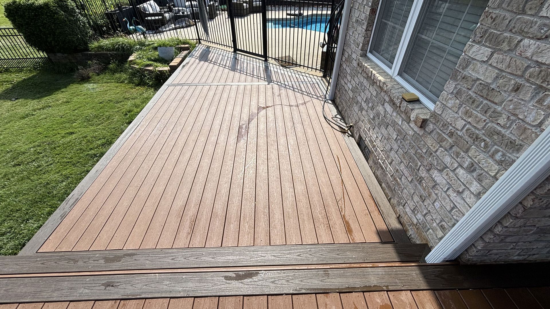 A wooden walkway leading to a brick house with a pool in the background.