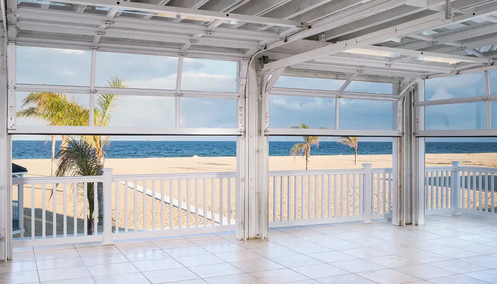 Bright beachfront patio with white railings, tiled floor, and ocean view through large windows