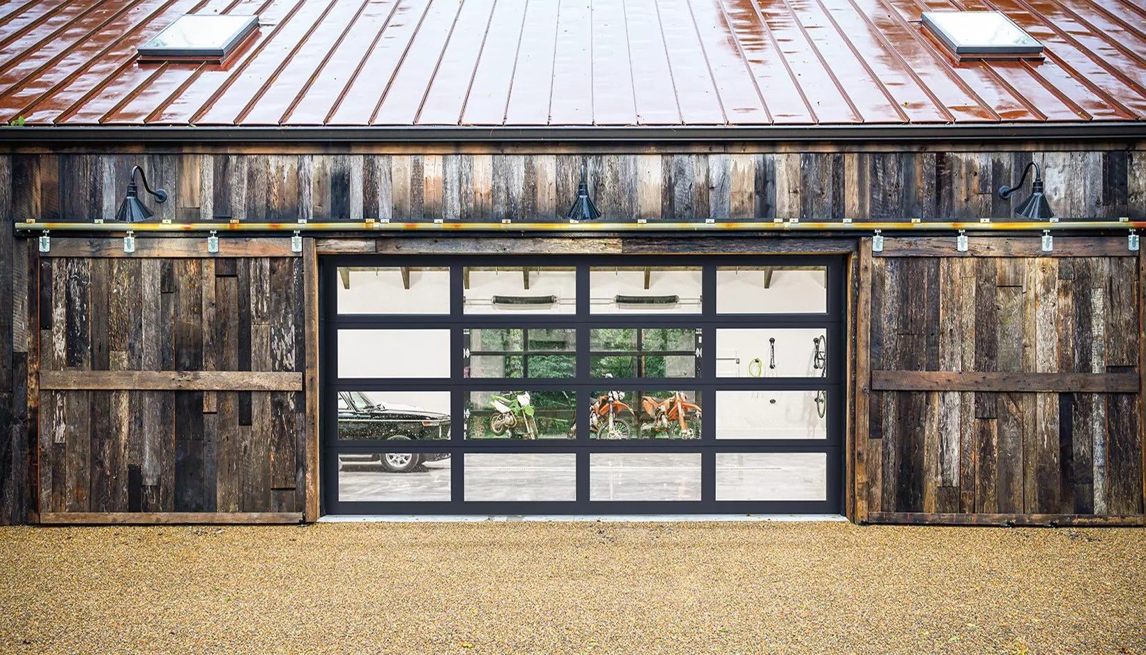 Modern glass garage door framed by rustic, weathered wood sliding barn doors under a copper roof.
