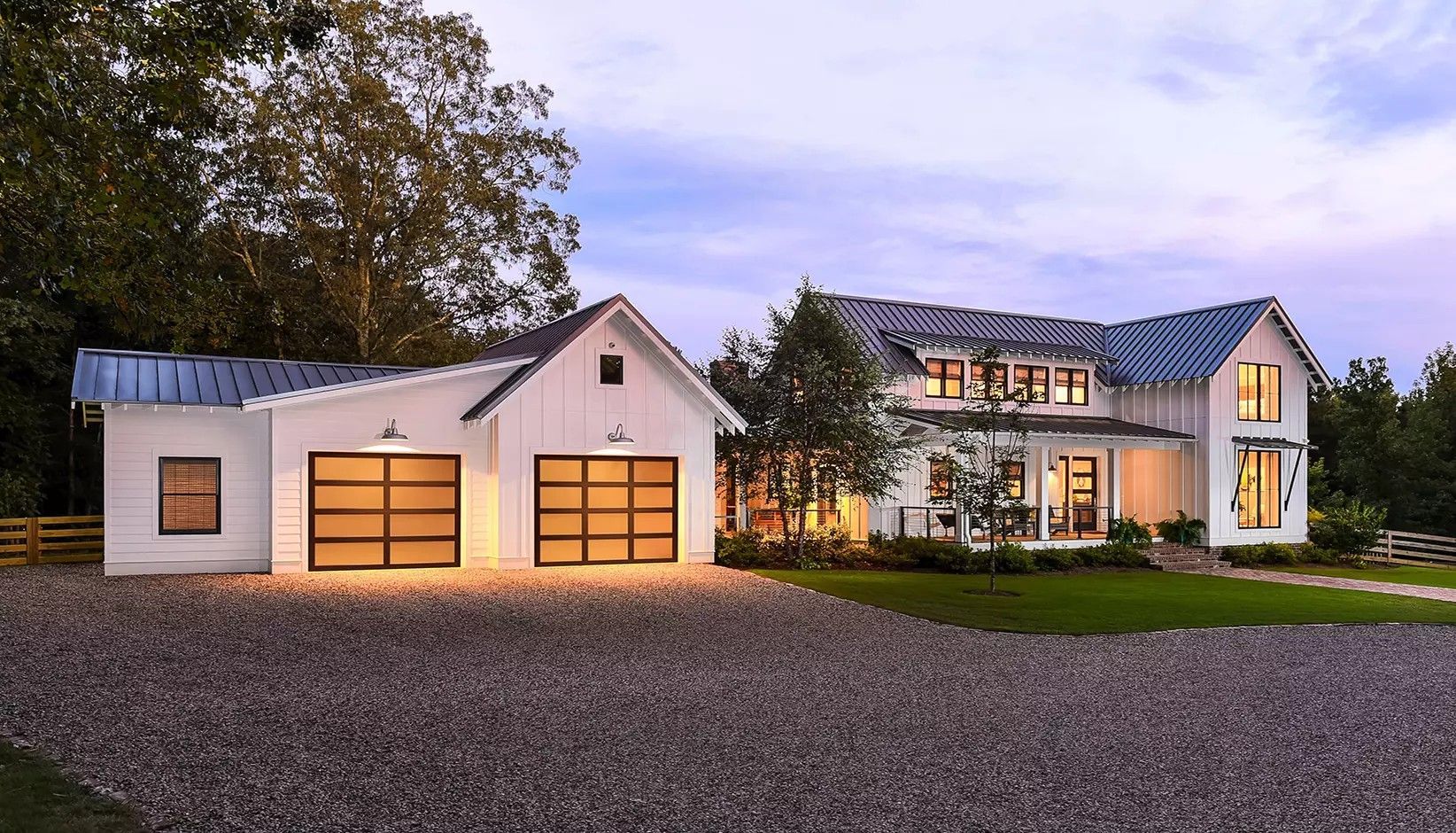 A white modern farmhouse with a gravel driveway, two-car garage, and dark-framed windows at twilight.