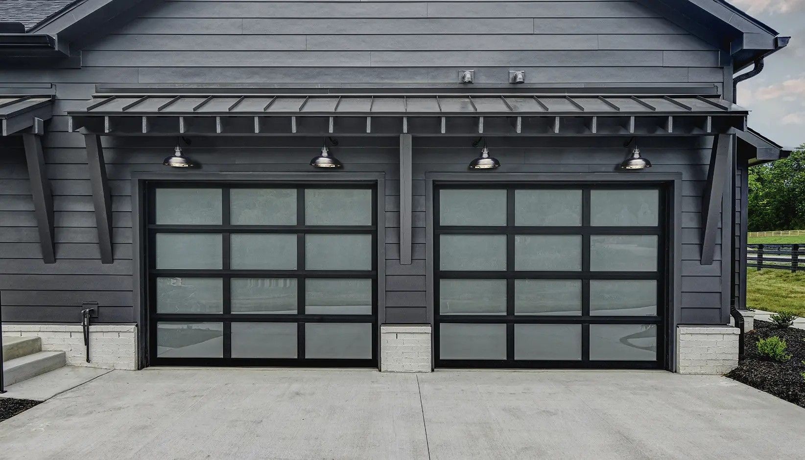Two modern garage doors with frosted glass panels and black frames set in a dark-sided home exterior.