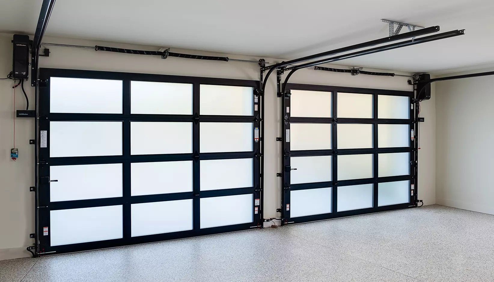 Two side-by-side modern garage doors with black frames and frosted glass panels inside a clean, speckled-floor garage.