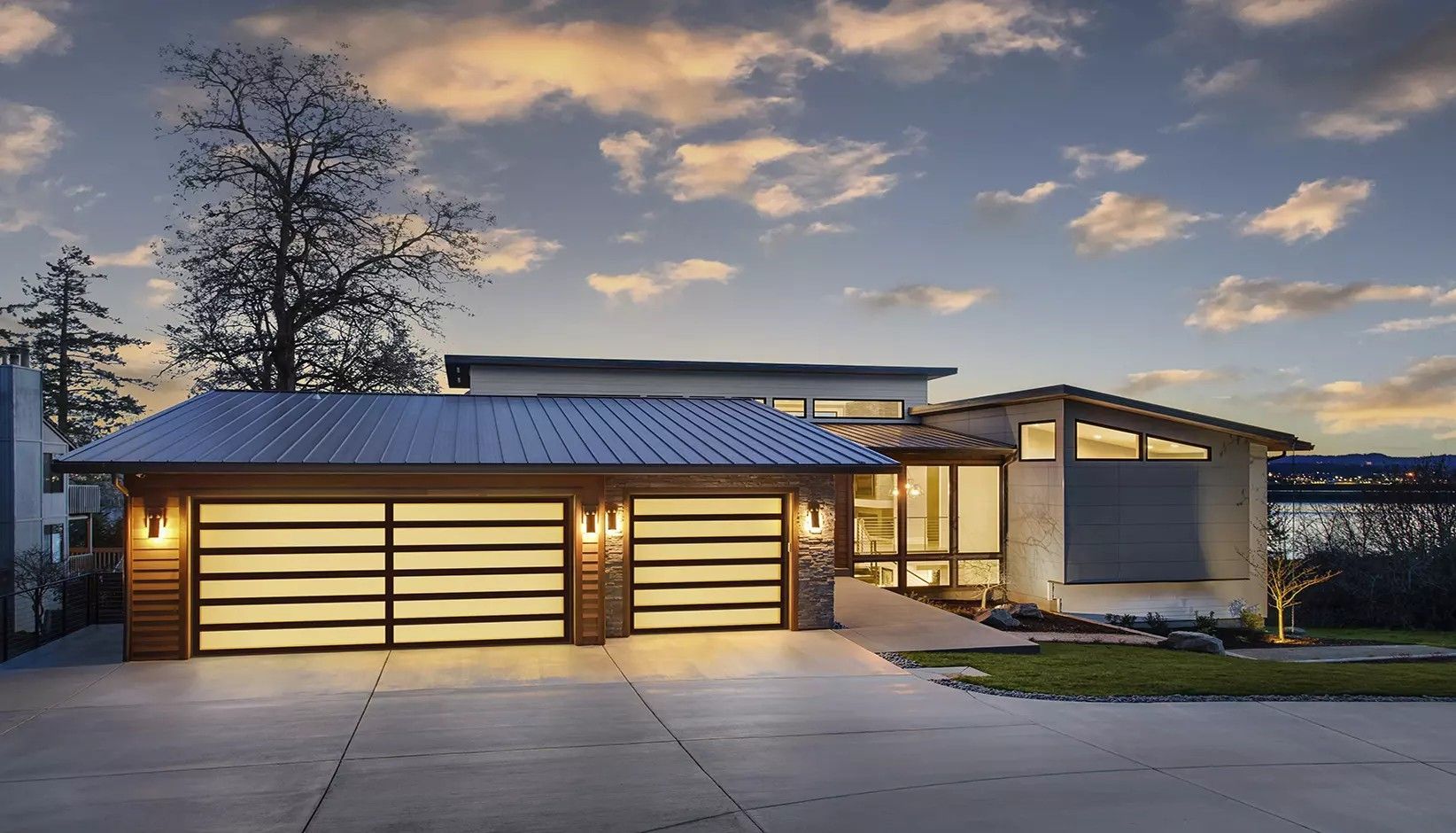 Modern house with illuminated horizontal panel garage doors at twilight under a cloudy sky.