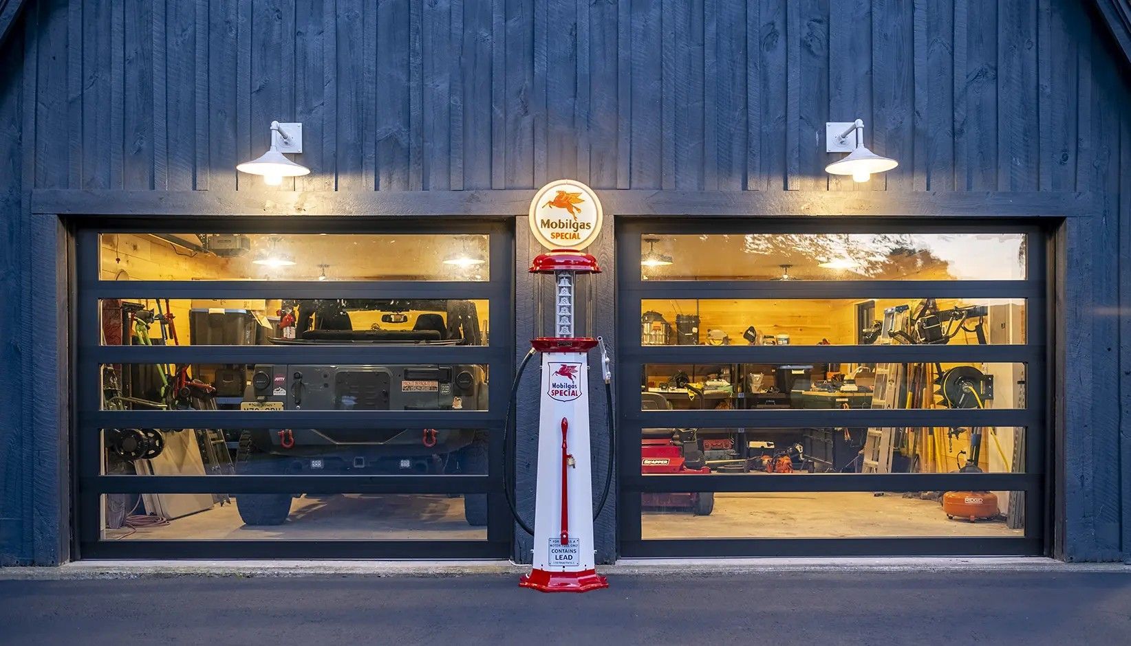 A dark blue wooden garage building with two glass-paneled doors and a vintage red and white fuel pump between them.