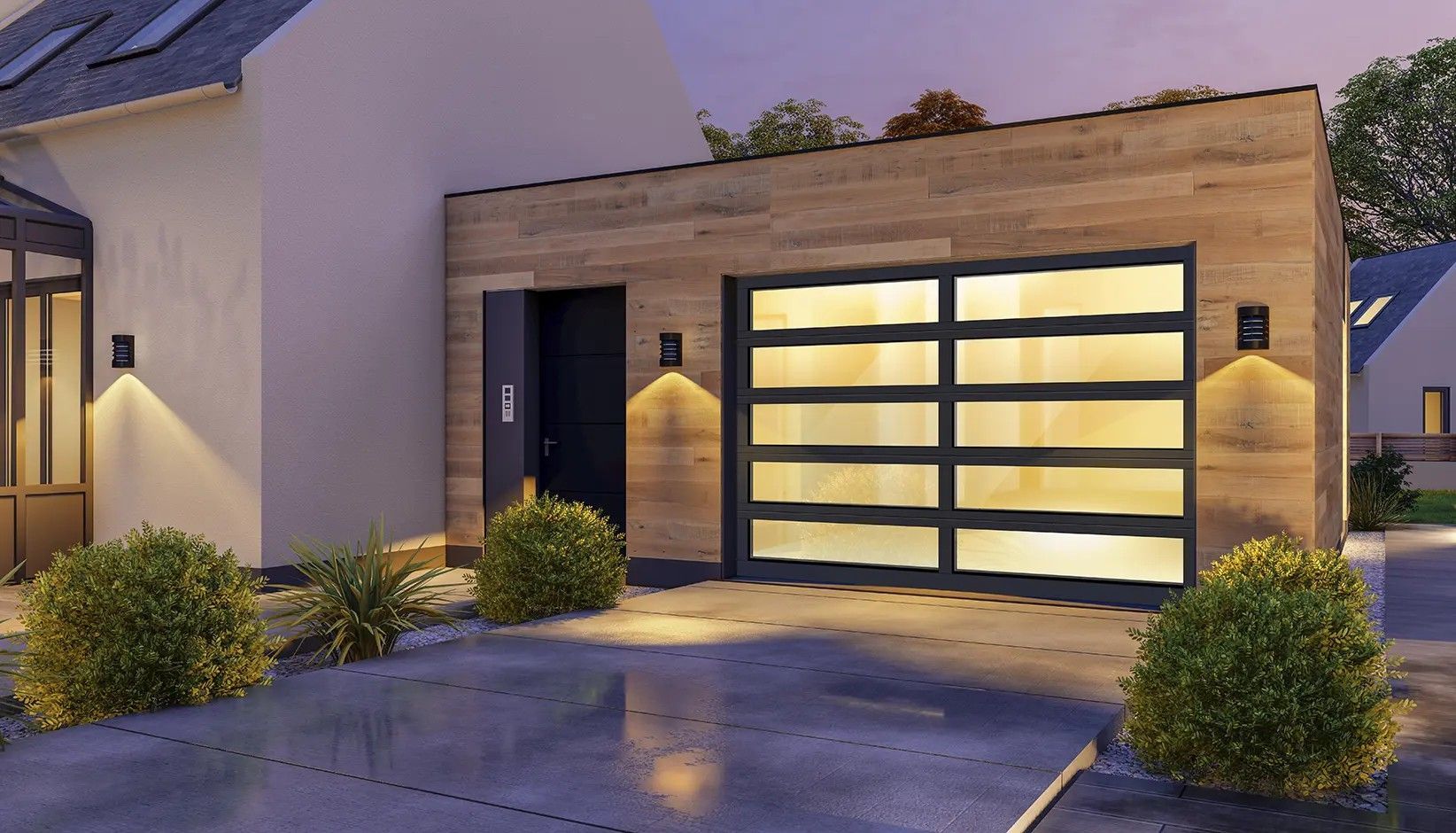 A modern house extension with wood-paneled walls, a large glass garage door, and glowing exterior wall lamps at dusk.