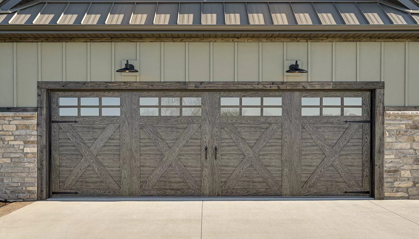 A wide, dark wood-finish garage door with cross-buck detailing and top windows, framed by stone siding.