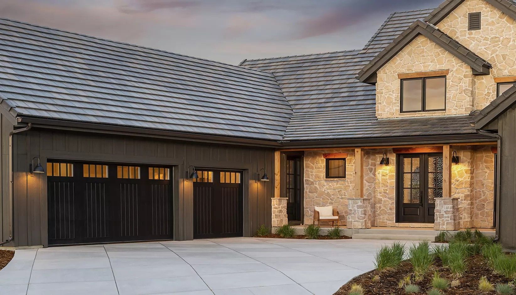 A modern home exterior with dark grey vertical siding, a stone facade, a dark shingled roof, and a three-car garage.