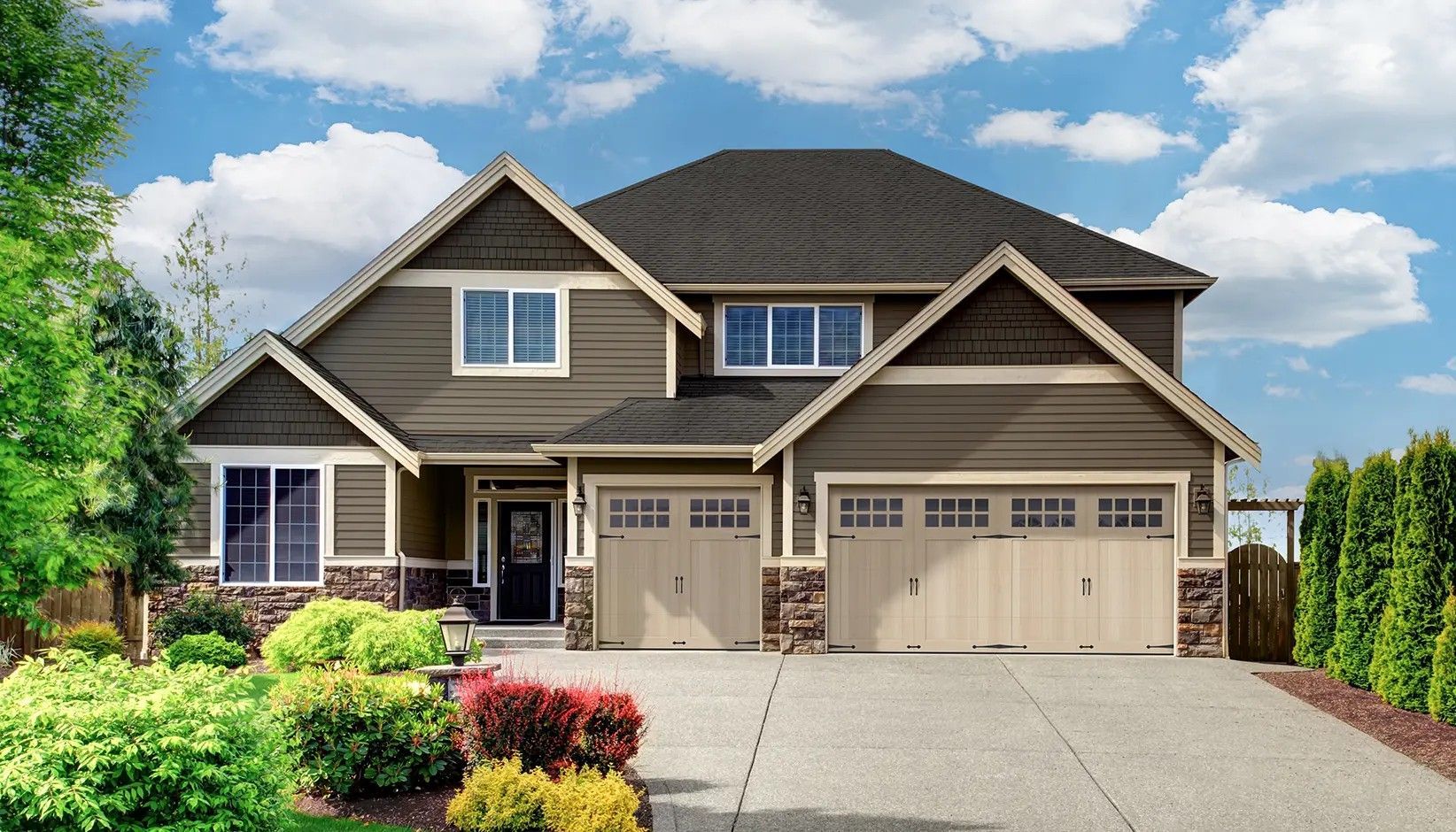 A two-story suburban home with brown horizontal siding, stone accents, a three-car garage, and a landscaped front yard.