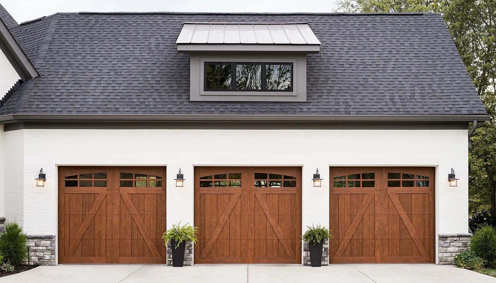 A three-car garage with white walls, stone accents, dark wooden carriage-style doors, and a dormer window on the roof.