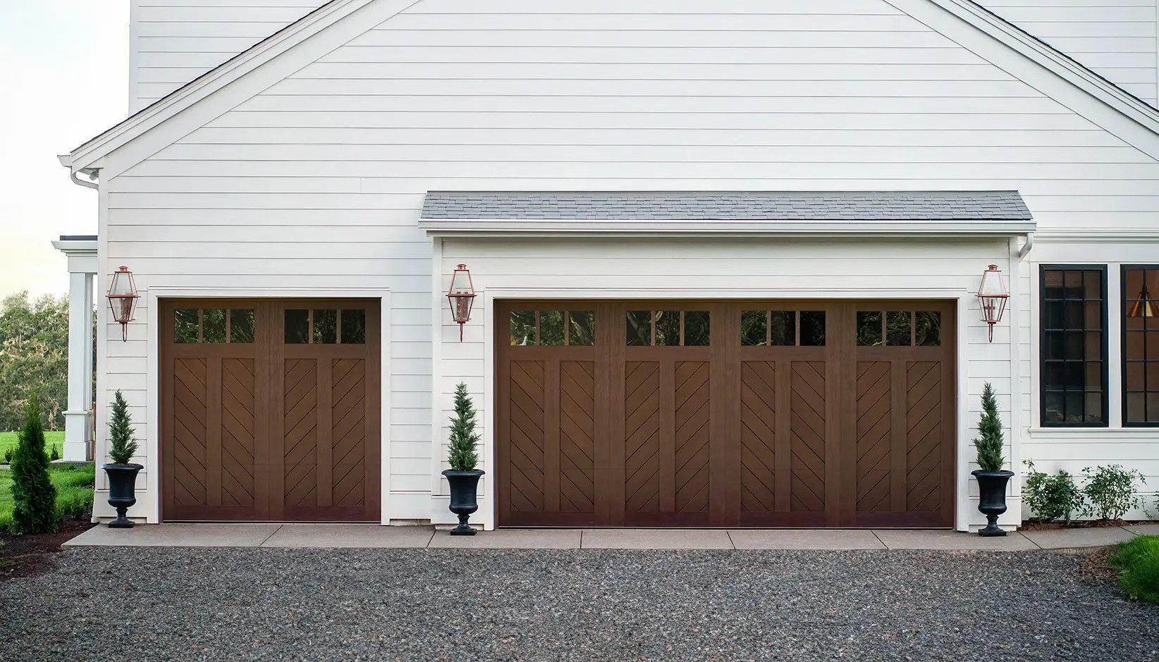 A white home with two brown garage doors featuring chevron wood paneling and rectangular windows at the top.