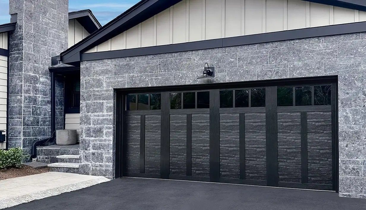 Modern garage with dark stone facade, black trim, and a matching black multi-panel garage door with top window row.