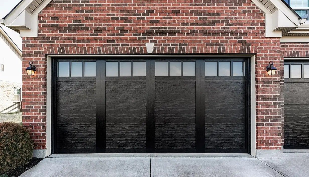 A black, multi-panel residential garage door with top-row windows, set into a red brick house exterior.