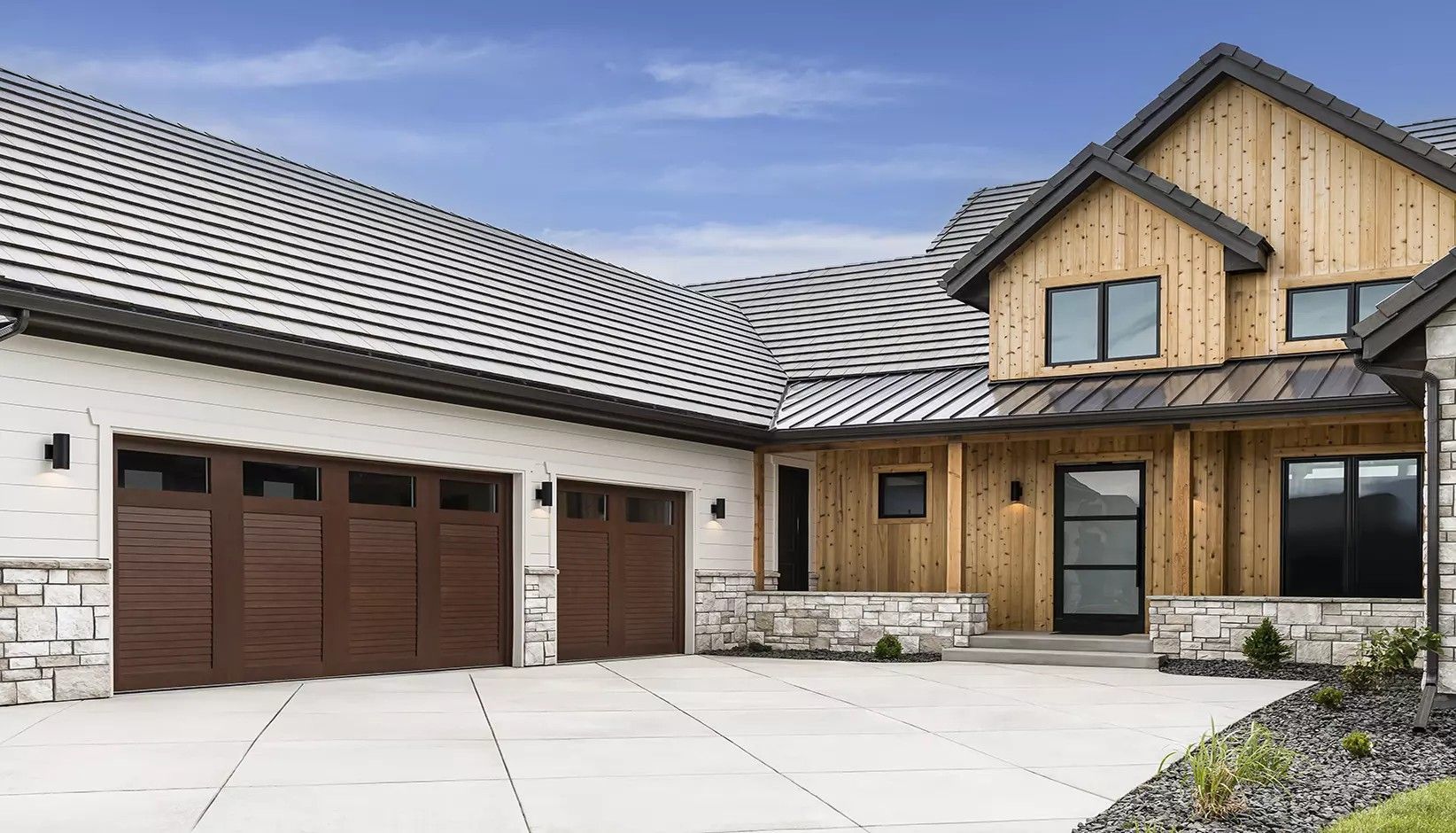 A modern suburban home featuring a wood-paneled exterior, a two-car garage, stone masonry base, and a concrete driveway.
