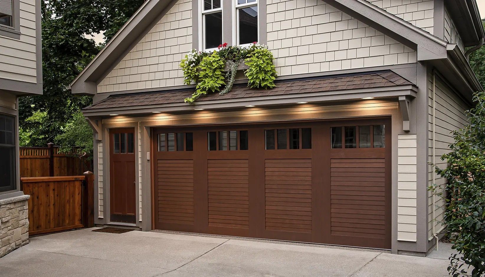 A detached garage with a dark brown carriage-style door, a matching side door, and exterior lighting under the roofline.