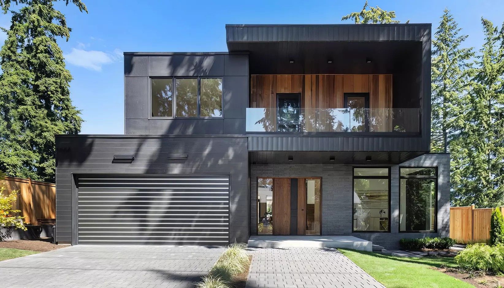 Modern two-story house with black exterior siding, a wooden accent balcony, and a multi-car garage on a landscaped lot.